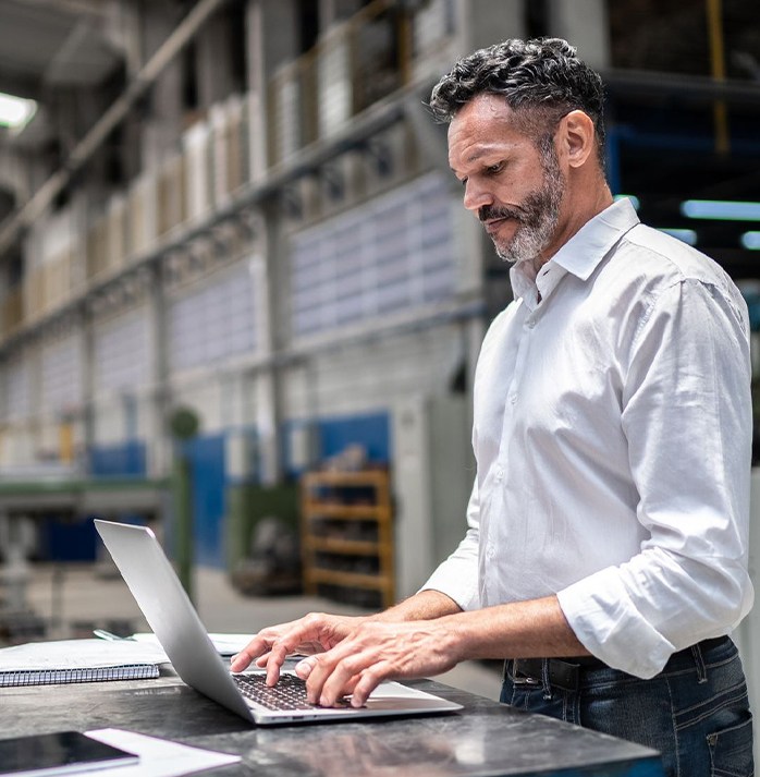 Man in a white shirt working on a laptop in an industrial factory setting
