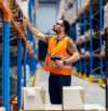Warehouse worker in an orange safety vest using a barcode scanner to manage inventory on high shelves